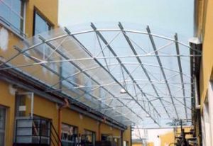 Tettoia in acciaio con travi reticolari e copertura in traslucido, volta a botte.